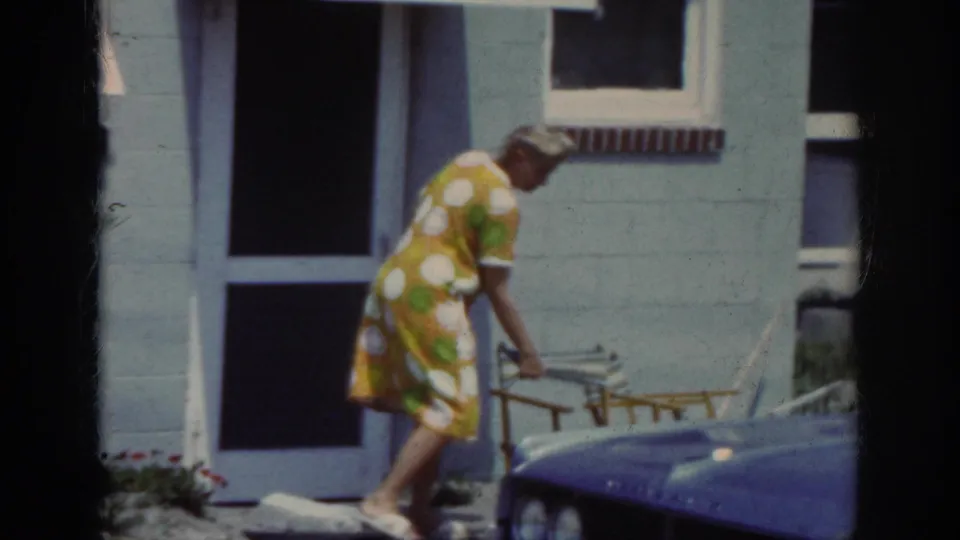 In the final frame, the woman bends toward the porch chair beside the light blue house, with the dog no longer clearly visible.