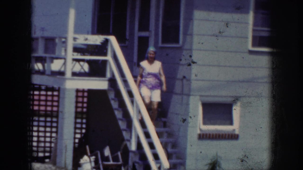 In Raleigh 1962 home-movie footage, a woman in a blue headscarf and white shorts steps down outdoor stairs by a house.