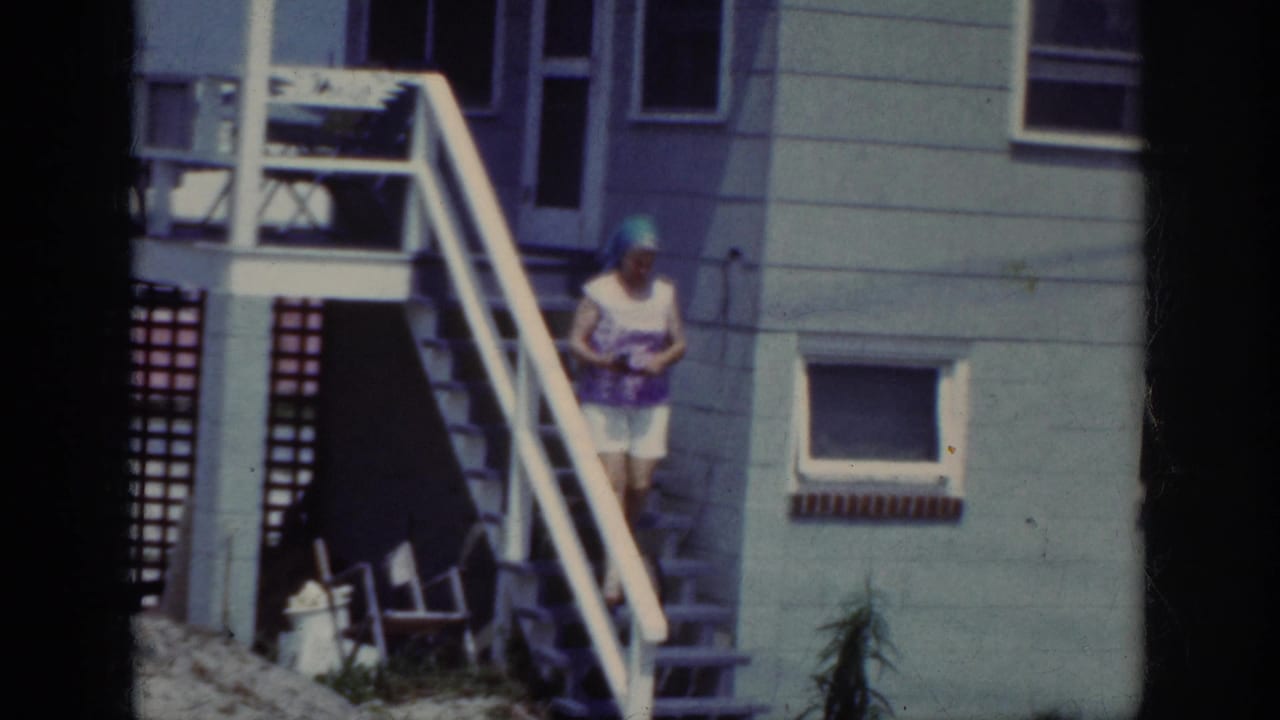 The woman descends the house stairs in Raleigh, wearing a blue headscarf, patterned top, and white shorts.