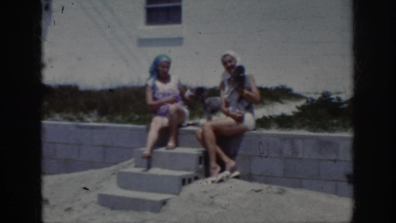 In 1962 home-movie footage, two women sit on concrete steps at a sandy beach area in Raleigh, North Carolina metadata context.