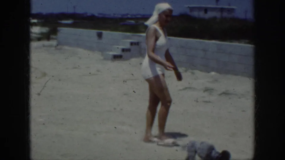 1962 Raleigh frame with the woman in a white swimsuit pausing on a sandy terrace while a small dog explores nearby.