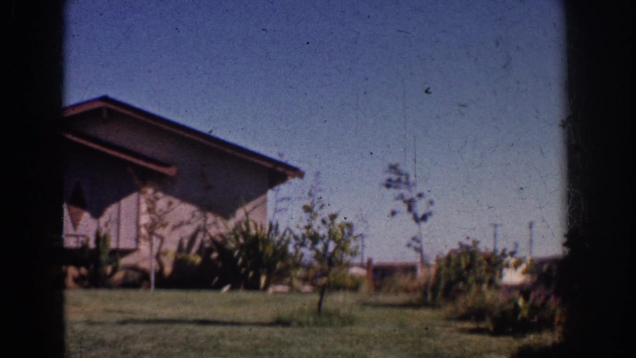 1962 Yorba Linda home-movie frame showing a mid-century house, lawn, small trees, and shrubs in bright daylight.