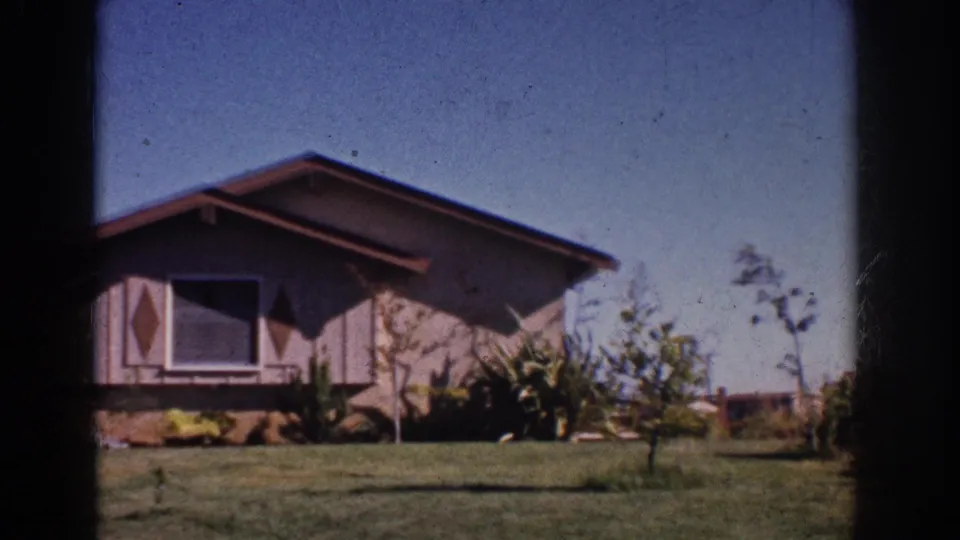 1962 Yorba Linda frame showing the house facade with diamond-patterned panels, window, lawn, and shrubs.