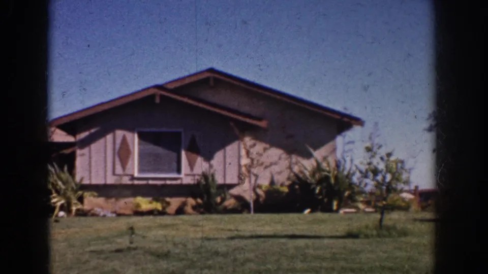 1962 Yorba Linda home-movie frame of a mid-century house front, lawn, shrubs, and small tree in sun.