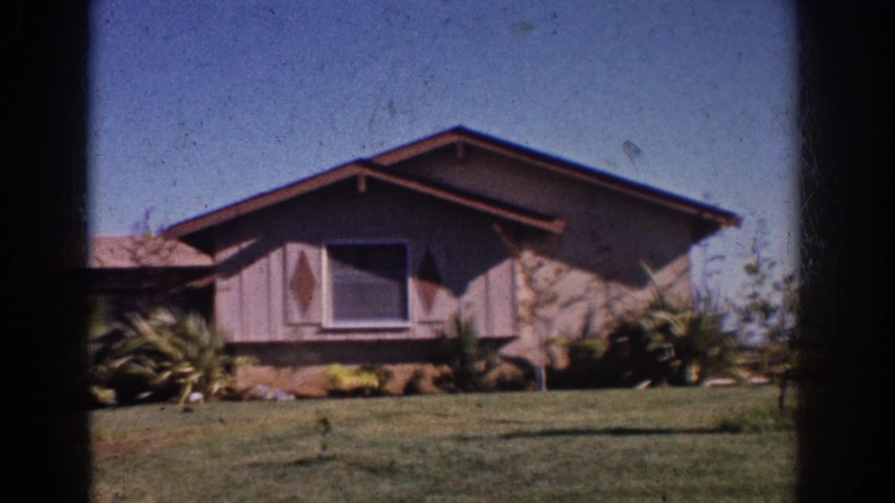 1962 Yorba Linda home-movie frame showing a mid-century ranch house, front lawn, shrubs, and palm-like landscaping under blue sky.