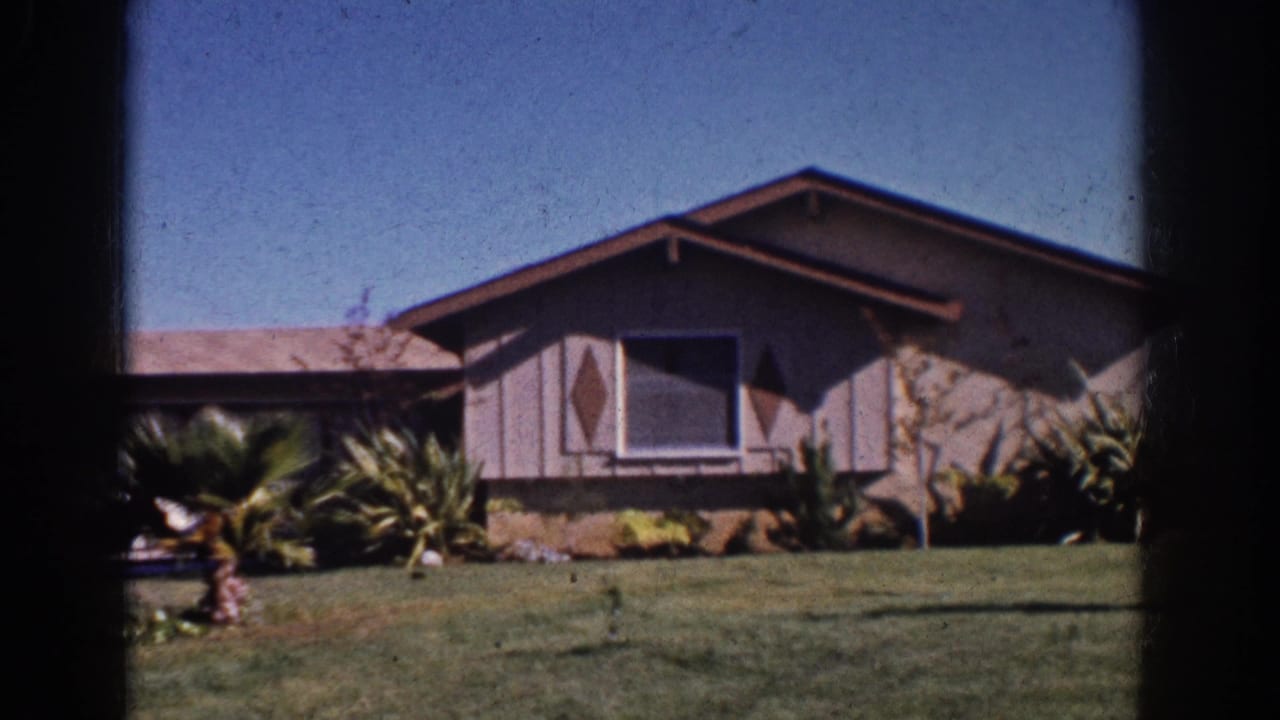 1962 Yorba Linda frame with a ranch-style house, diamond window accents, lawn, shrubs, and a small palm-like plant near the driveway.