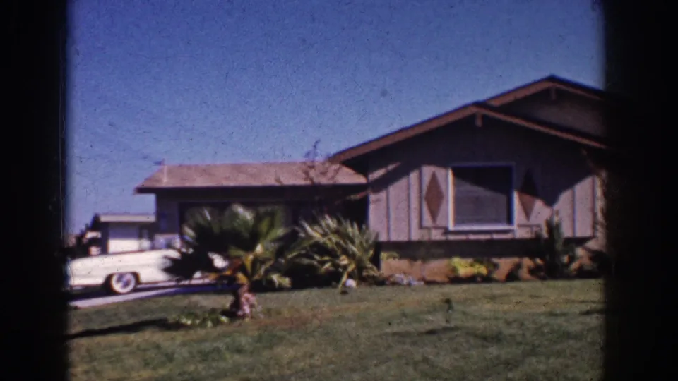1962 Yorba Linda frame with a white American sedan parked or passing in the driveway beside a mid-century ranch-style house.