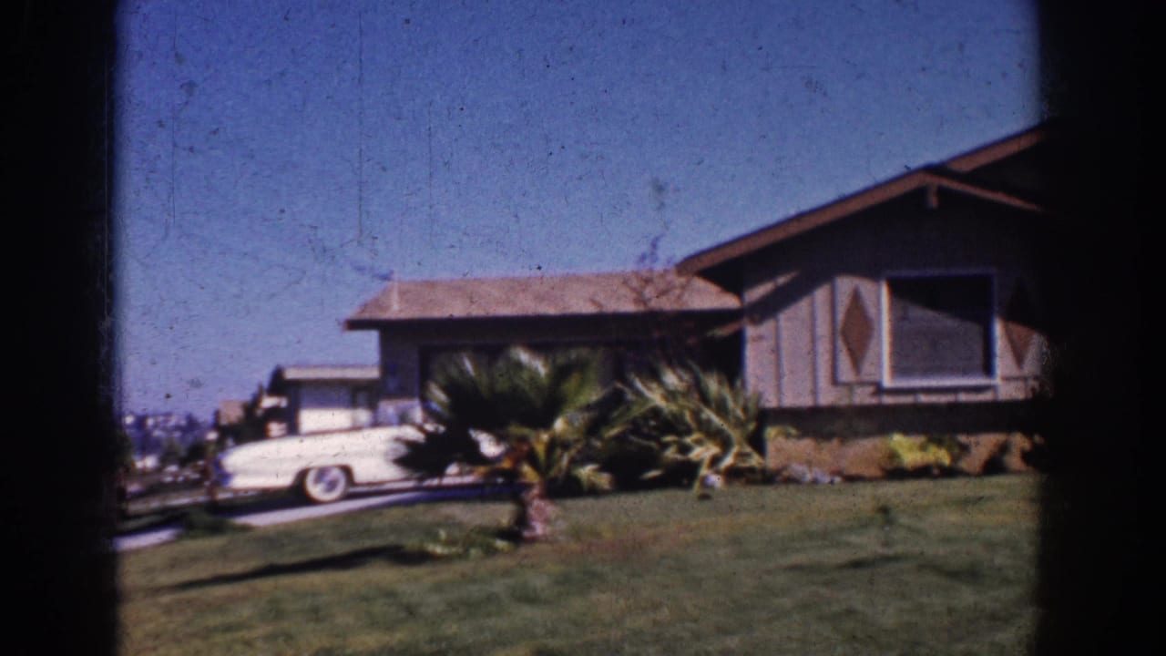 1962 Yorba Linda suburban home view with a white mid-century car in the driveway, lawn, and palm-like landscaping.