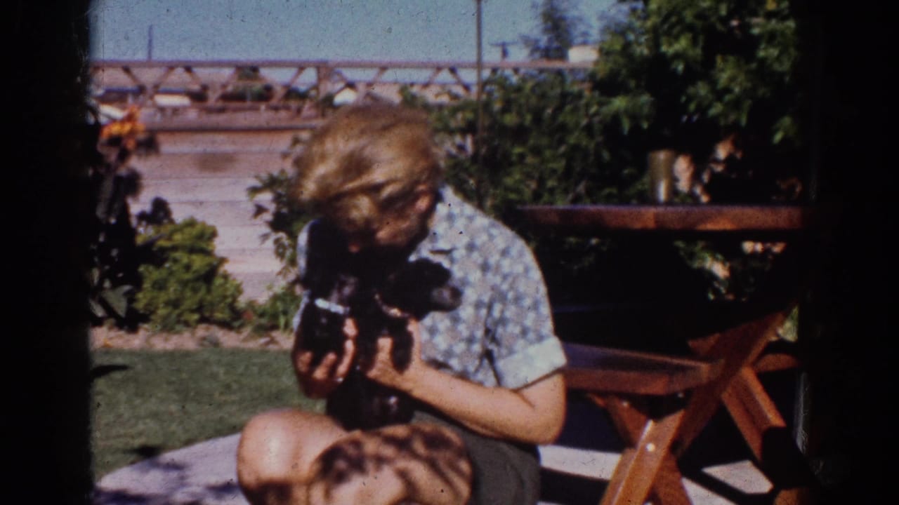 In a Yorba Linda backyard, the young person holds the black puppy close beside a picnic table and garden shrubs.