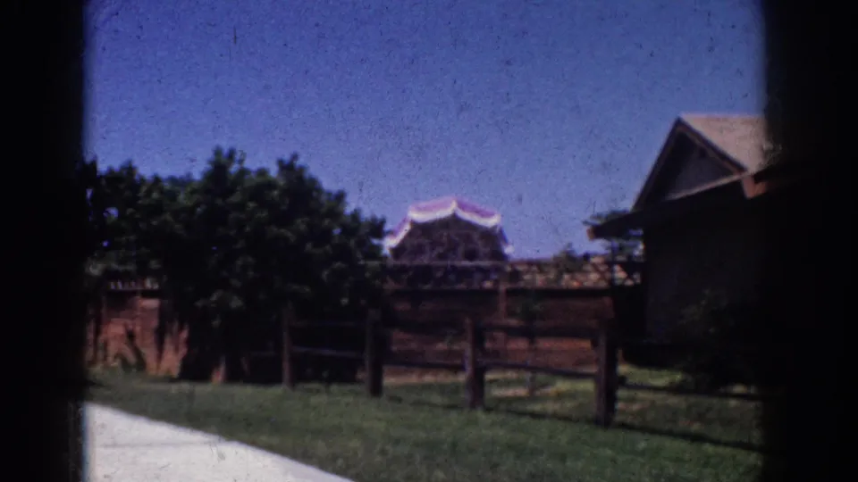 After a dark transition, the 1962 Yorba Linda footage shows a wider residential yard with lawn, fencing, trees, and neighboring rooflines under a clear sky.