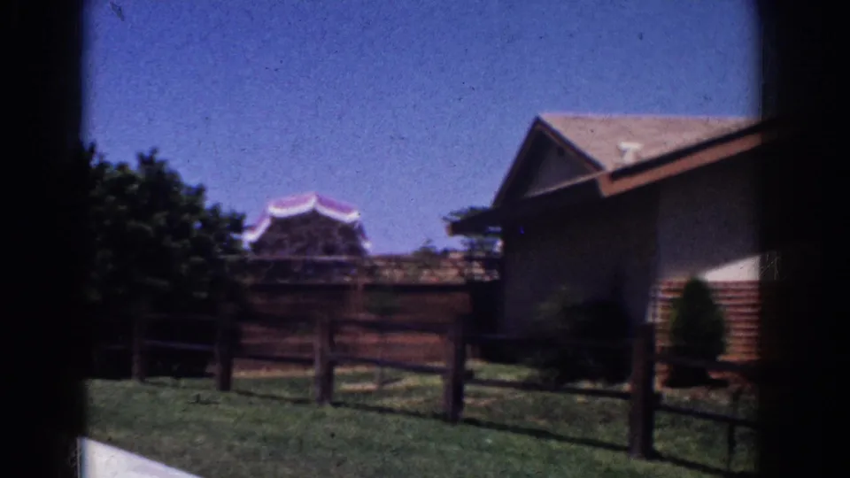 The final 1962 Yorba Linda frame holds on the backyard view, showing grass, a fence, trees, and adjacent houses in bright daylight.