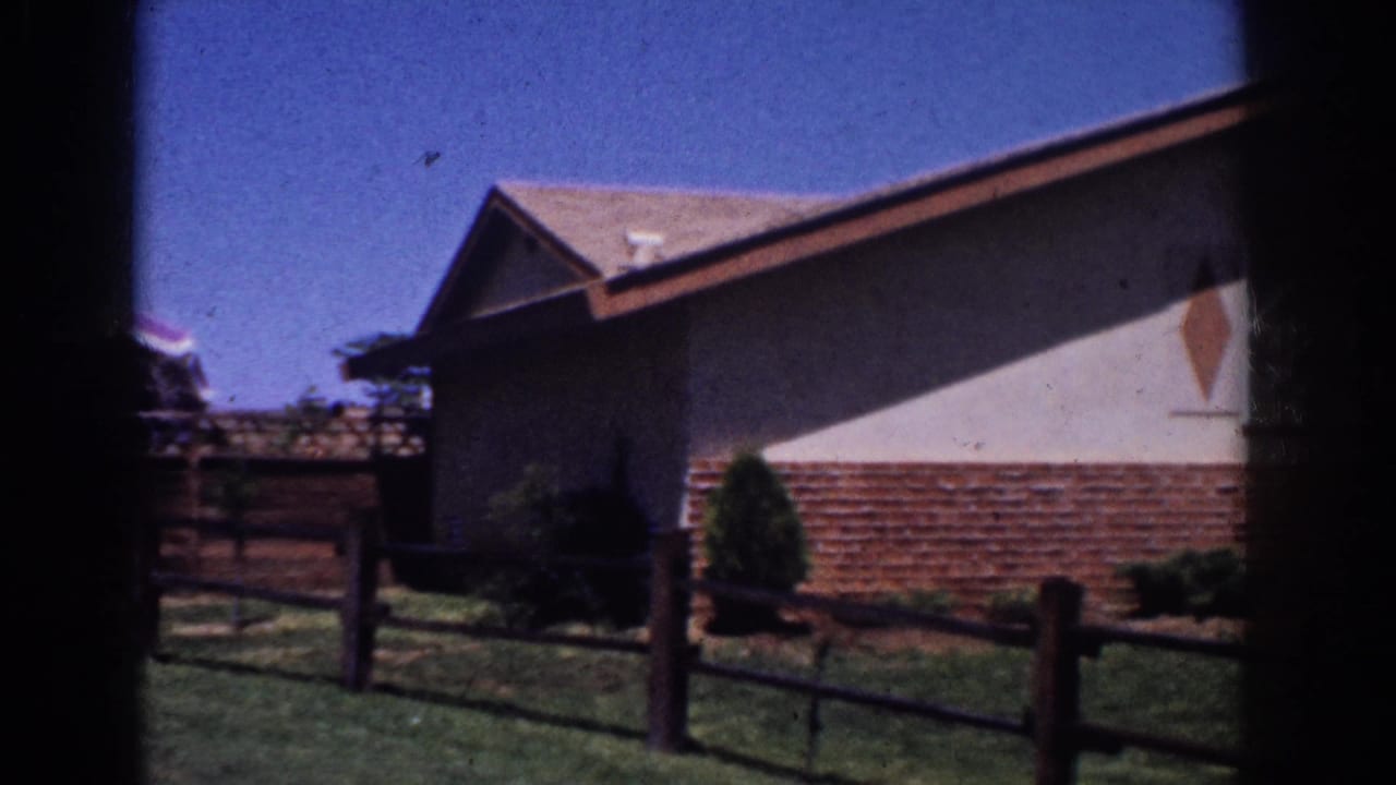 1962 Yorba Linda frame centered on the side of a mid-century ranch home with brick base, stucco wall, fence, and lawn.