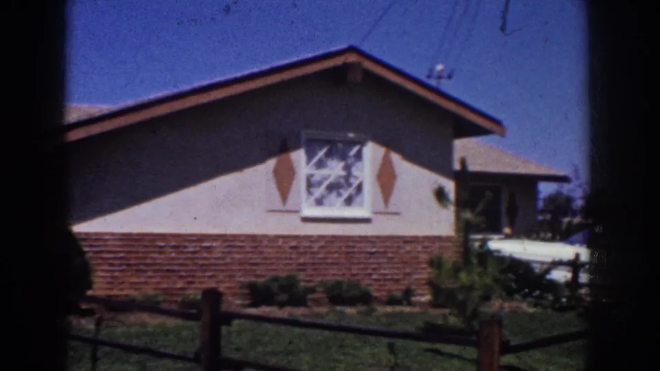 1962 Yorba Linda frame of a ranch-style home exterior with a shuttered window, brick lower wall, fence, lawn, and partial side structure.