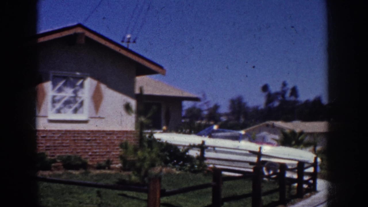1962 Yorba Linda suburban exterior with a stucco cottage, brick base, driveway car, fence, lawn, and clear sky.