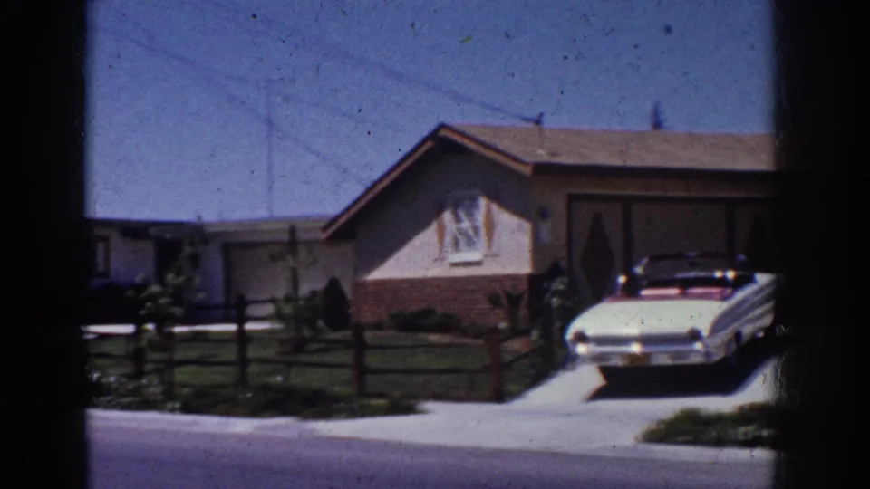 Yorba Linda suburban driveway in 1962 with a white convertible, single-story home, lawn, fence, and utility lines under clear sky.