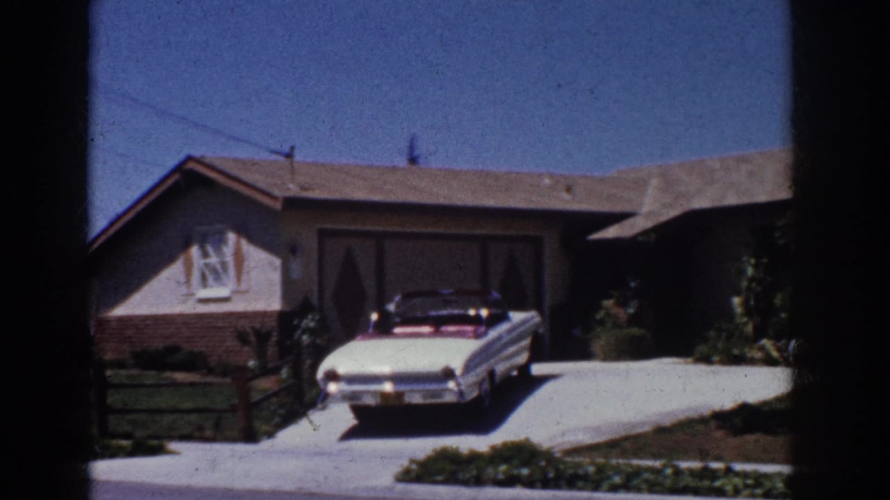 White convertible near a garage with lawn, shrubs, and house facade visible.