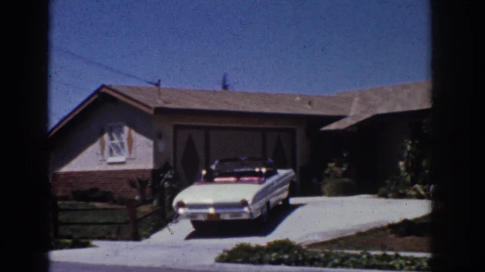 1962 Yorba Linda frame with a white convertible on a driveway beside a low suburban house, lawn, and front landscaping.