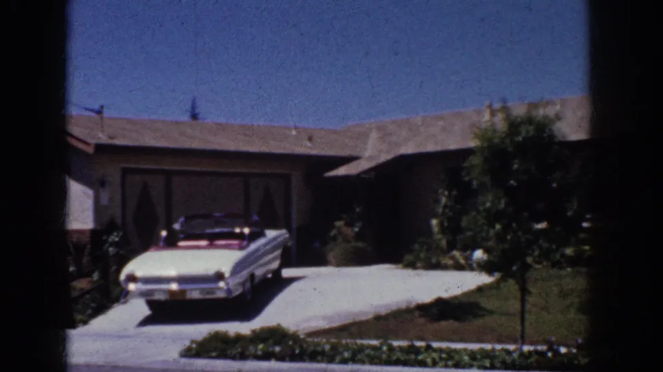 1962 Yorba Linda home-movie frame showing the white convertible, driveway, low house, lawn, planting bed, and small tree.