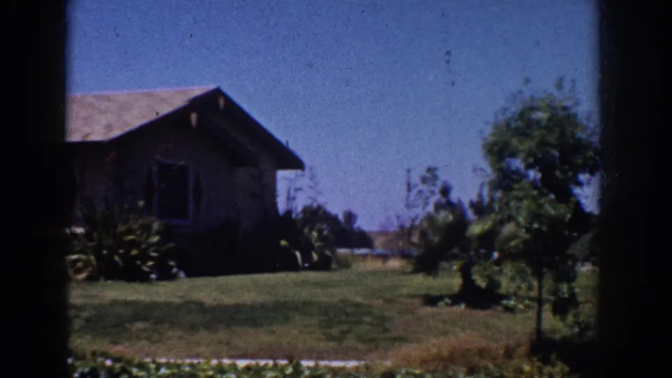 Late frame from the 1962 Yorba Linda pan showing the ranch house, landscaped yard, small tree, and open blue sky.
