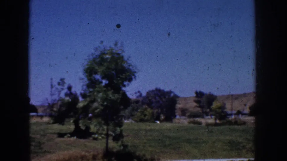 1962 Yorba Linda 8mm frame showing a grassy yard, trees, distant hills, and blue sky through a shaded window or doorway edge.