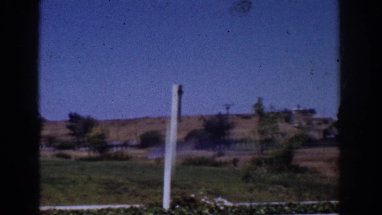 1962 Yorba Linda view across a lawn toward dry hills, scattered trees, utility lines, and low homes, framed by dark window edges.