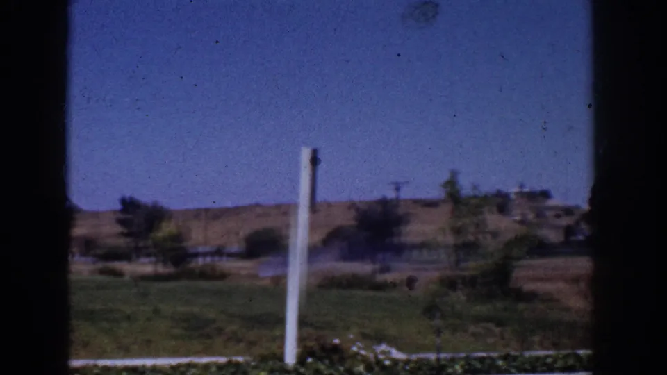 1962 Yorba Linda view across a lawn toward dry hills, scattered trees, utility lines, and low homes, framed by dark window edges.