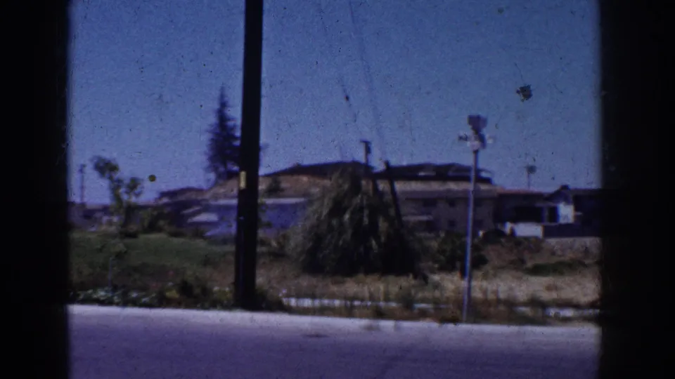 1962 Yorba Linda suburban view with utility poles, a low building, trees, lawn, and rolling dry hills beyond the window frame.