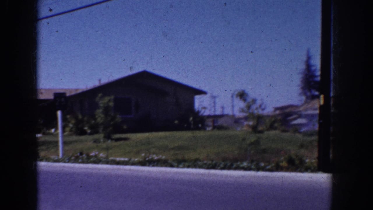 1962 Yorba Linda street view showing a low suburban house, green lawn, curb, shrubs, and overhead line through dark film-edge framing.