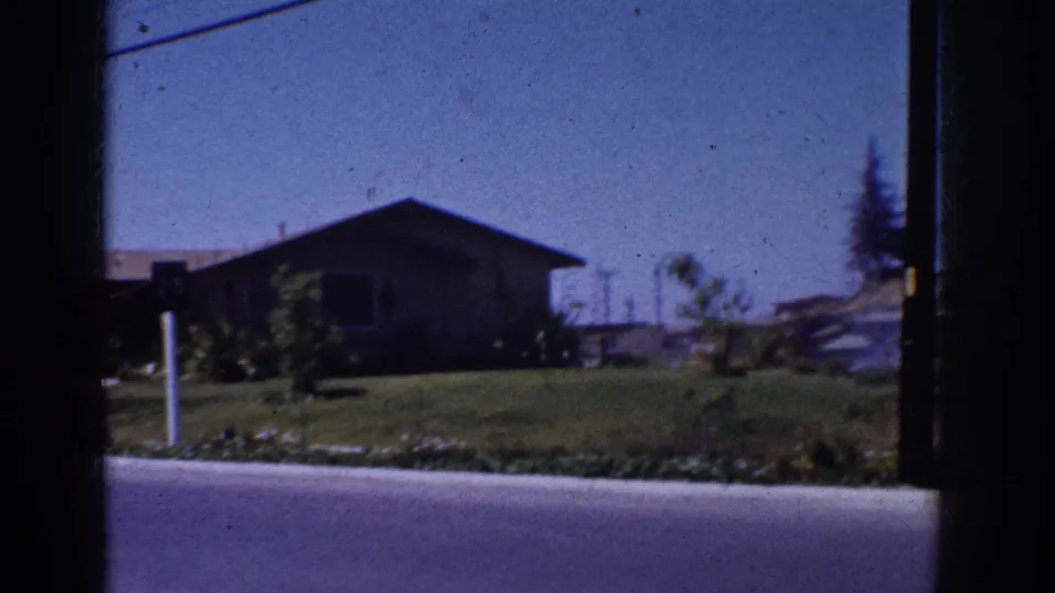 1962 Yorba Linda street view showing a low suburban house, green lawn, curb, shrubs, and overhead line through dark film-edge framing.