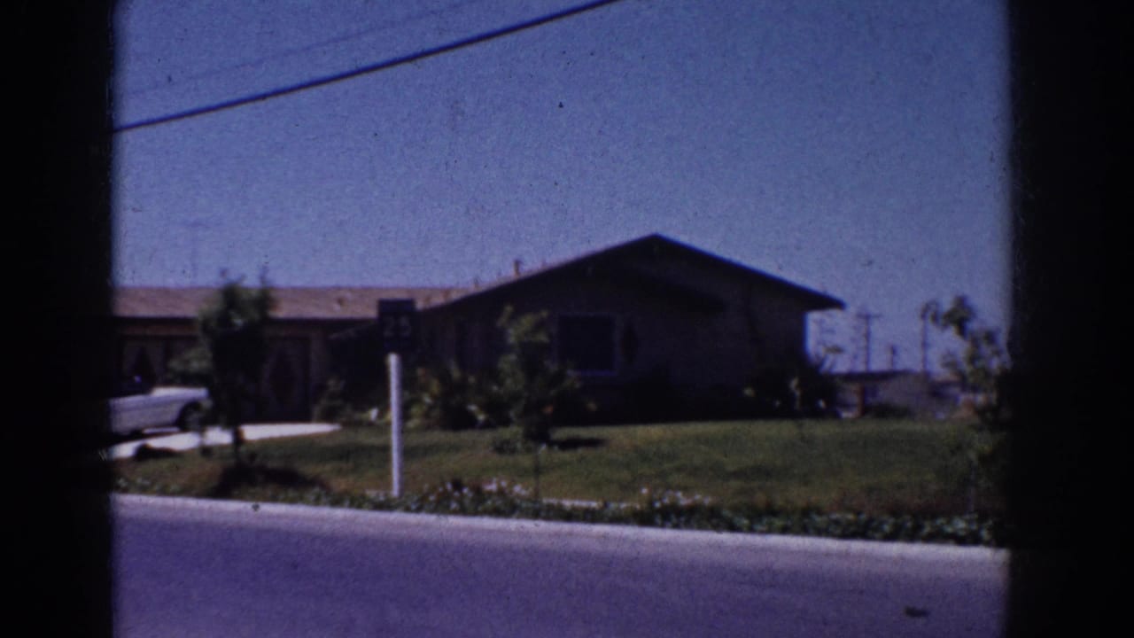 1962 Yorba Linda home-movie frame showing a single-story suburban house, front lawn, shrubs, curb, and partial white car.