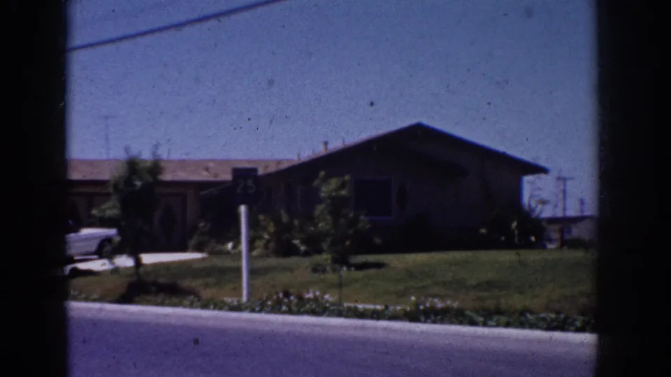 1962 Yorba Linda frame with a mid-century suburban house, 25 speed sign, green lawn, shrubs, and partial white convertible.