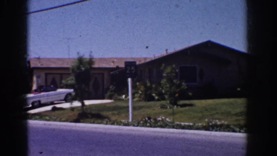 1962 Yorba Linda home-movie still showing a white classic convertible, 25 speed sign, front lawn, and single-story house.