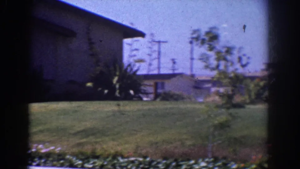 1962 Yorba Linda frame with the house partly cropped at left, a lawn and curb in front, shrubs and utility poles in the background.