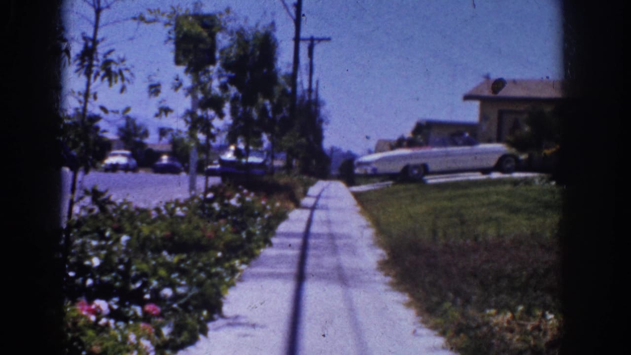 1962 Yorba Linda suburban sidewalk with flower beds, utility poles, trees, single-story homes, and a white car parked ahead.