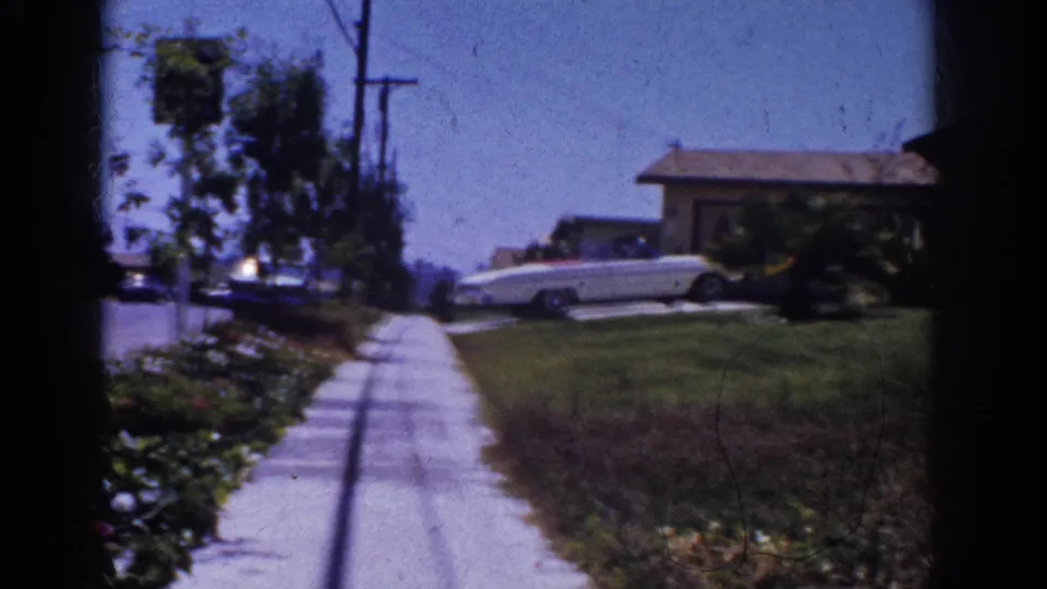 1962 Yorba Linda frame looking along a residential sidewalk toward a white convertible parked beside a single-story home.