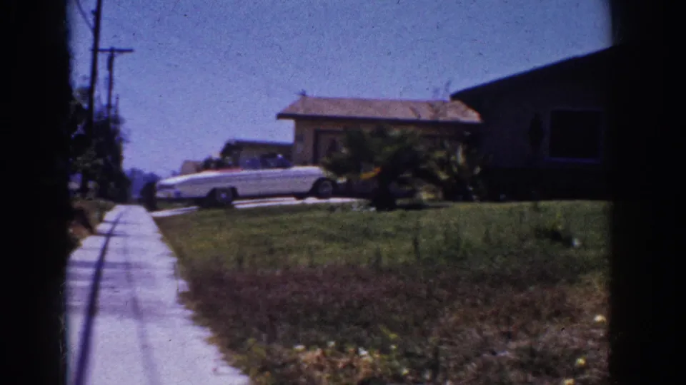 1962 Yorba Linda suburban exterior with a sidewalk, broad lawn, white convertible, and single-story home in bright sun.