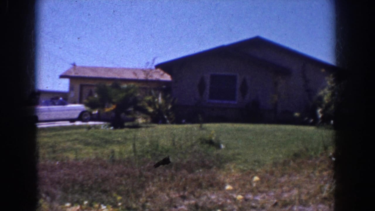 1962 Yorba Linda frame with a single-story home, broad lawn, shrubs, and part of a white convertible at the driveway edge.