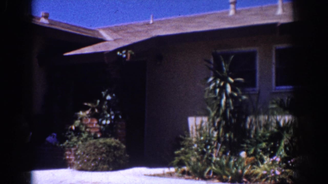 1962 Yorba Linda home-movie frame showing a single-story stucco house with garden plants and windows under a blue sky.