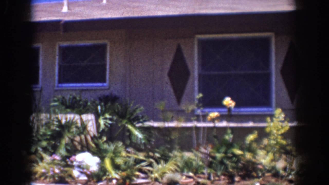 1962 Yorba Linda home-movie frame showing a mid-century house facade, windows, diamond shutters, and a planted garden.
