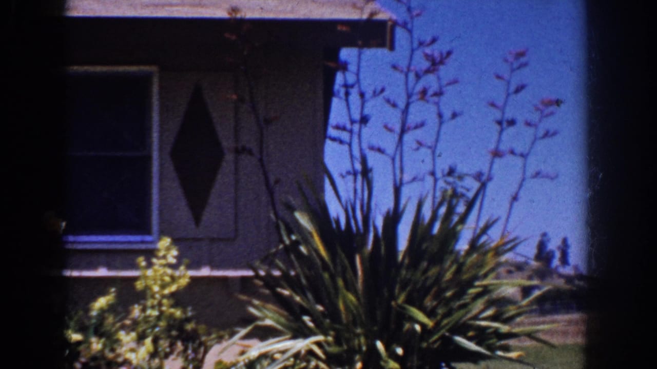 1962 Yorba Linda frame with a shaded house facade, diamond-shaped decoration, window, roof line, and sunlit garden plants.