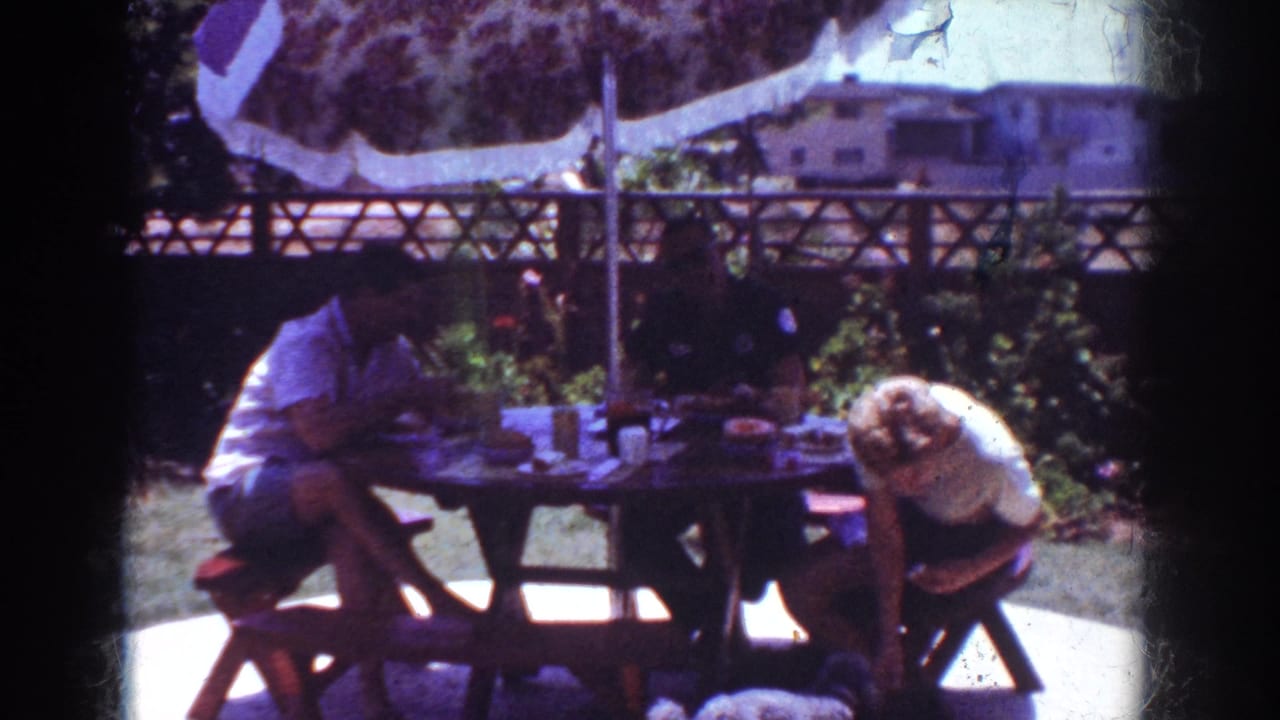 1962 Yorba Linda backyard picnic view with adults at a table, the blonde woman bending toward the seat or ground beside her.