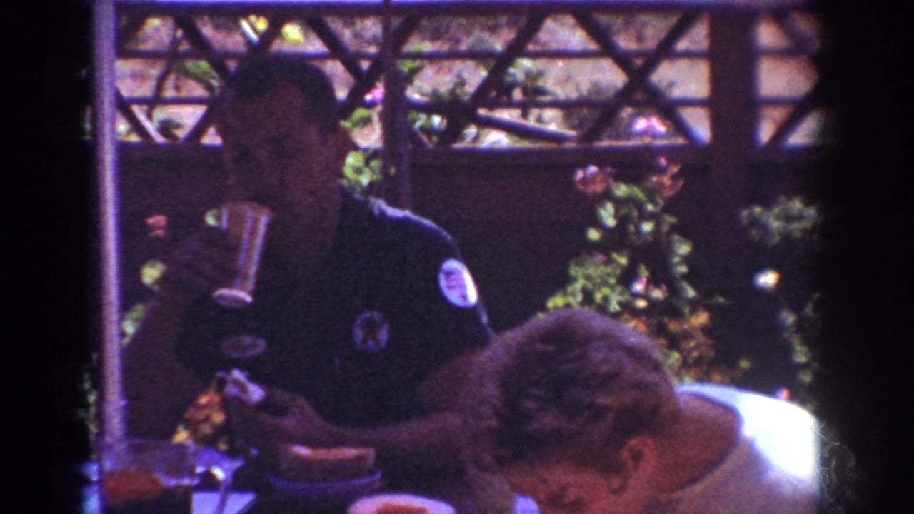 In 1962 Yorba Linda home-movie footage, an adult man in a dark shirt drinks at an outdoor patio table beside another seated man.