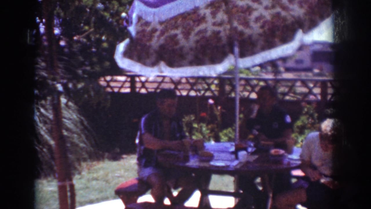 1962 Yorba Linda backyard scene with three adults gathered around a round picnic table under a fringed umbrella.
