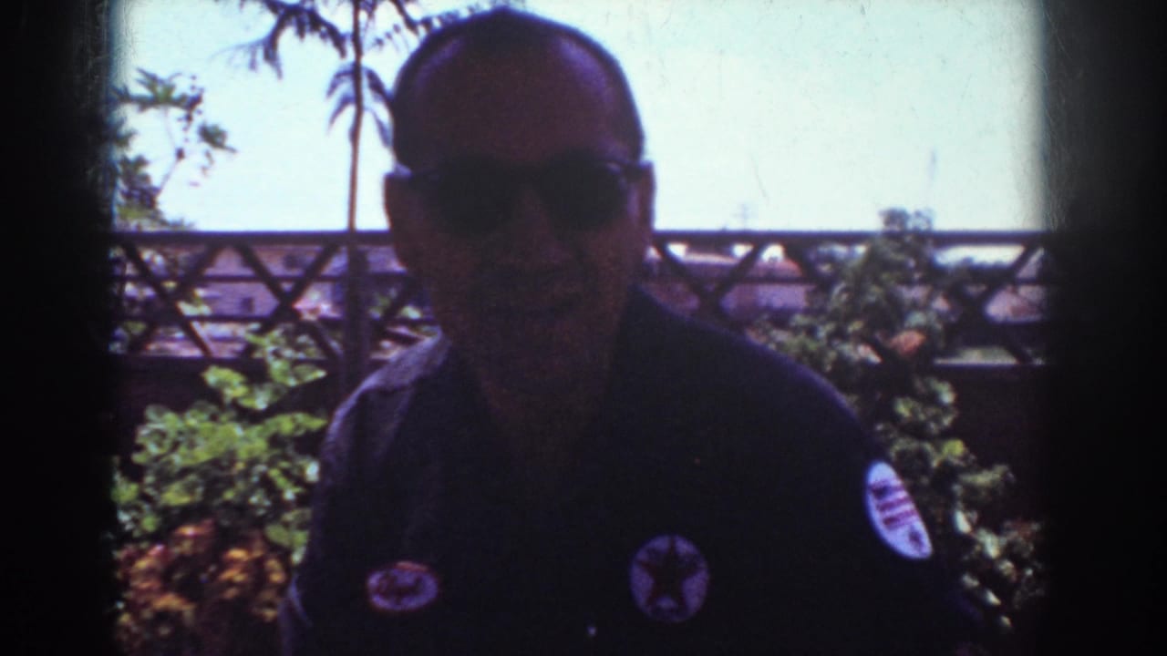 In 1962 Yorba Linda home-movie footage, a man in sunglasses stands near a backyard patio with shrubs and bright sky behind him.