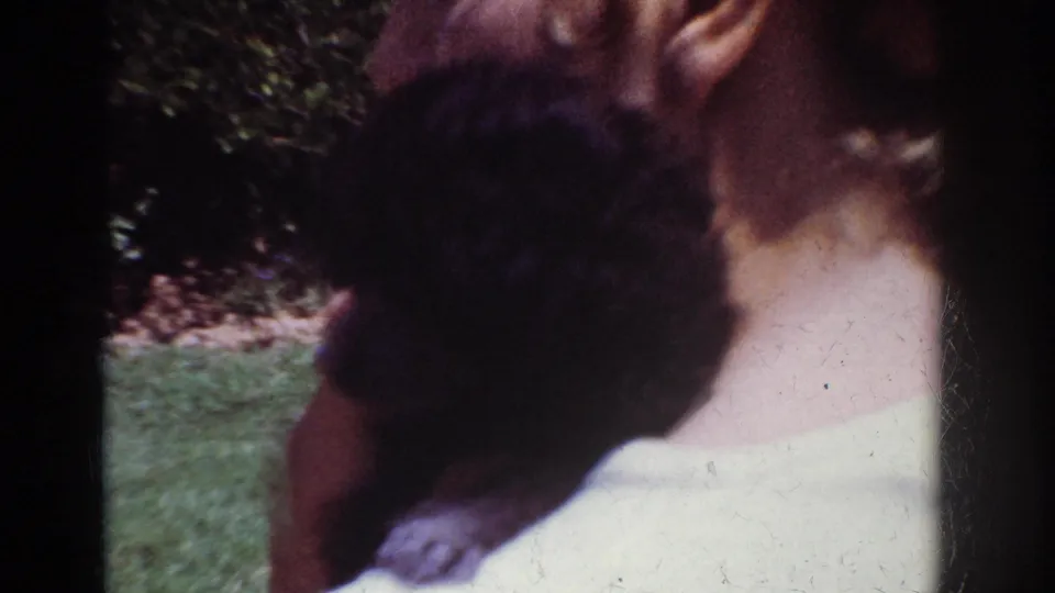 A woman in a light-colored top holds a small black puppy close to her shoulder in a sunny Yorba Linda backyard.