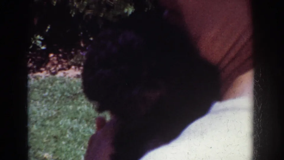 The home movie moves closer as the woman holds the fluffy black puppy against her shoulder on the backyard lawn.