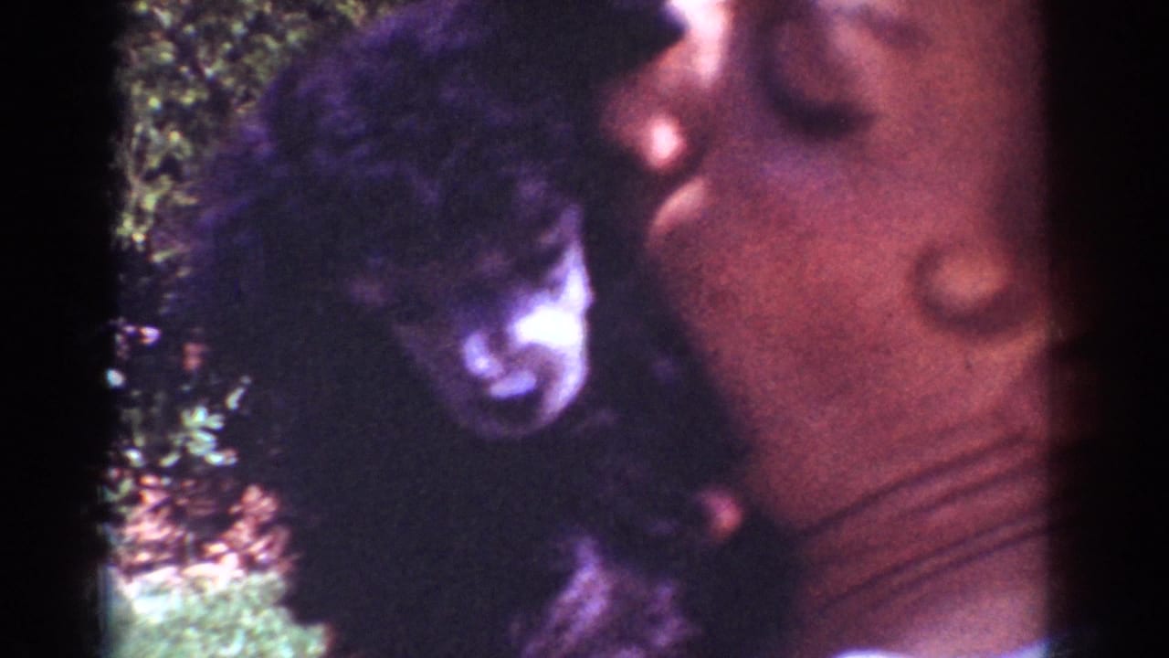1962 Yorba Linda home-movie frame showing a woman leaning near a small black puppy in a grassy yard.
