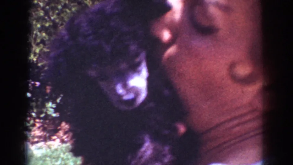 1962 Yorba Linda home-movie frame showing a woman leaning near a small black puppy in a grassy yard.