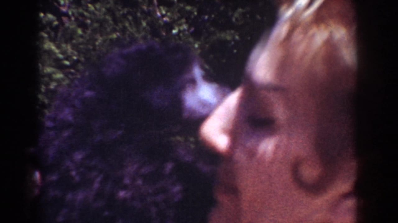 In 1962 Yorba Linda home-movie footage, a woman holds a small dark dog close and kisses its face outdoors.