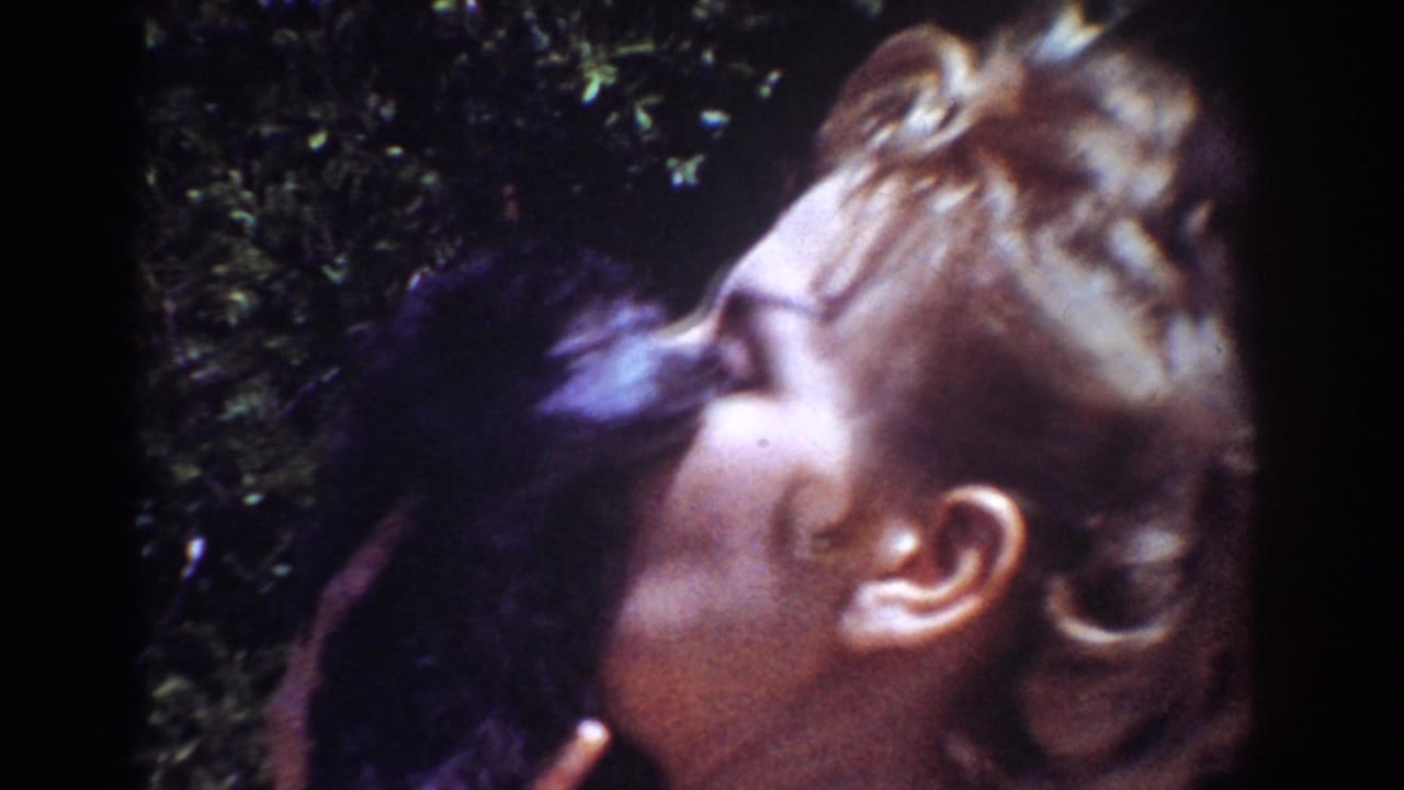 Blonde woman kisses a small black puppy while standing near leafy backyard plants.